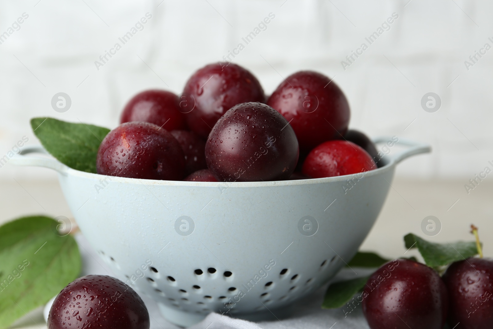 Photo of Ripe plums in colander on table, closeup