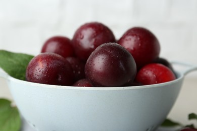 Photo of Ripe plums in colander on table, closeup