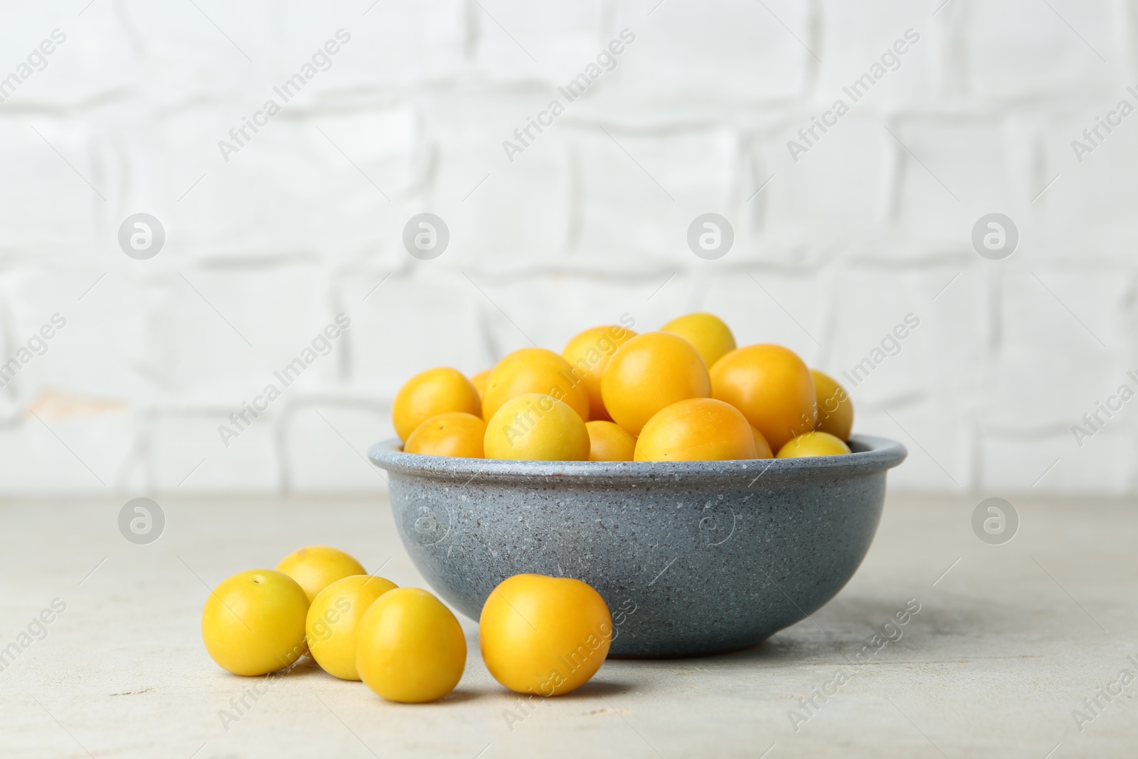 Photo of Ripe plums in bowl on light textured table