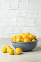 Photo of Ripe plums in bowl on light textured table