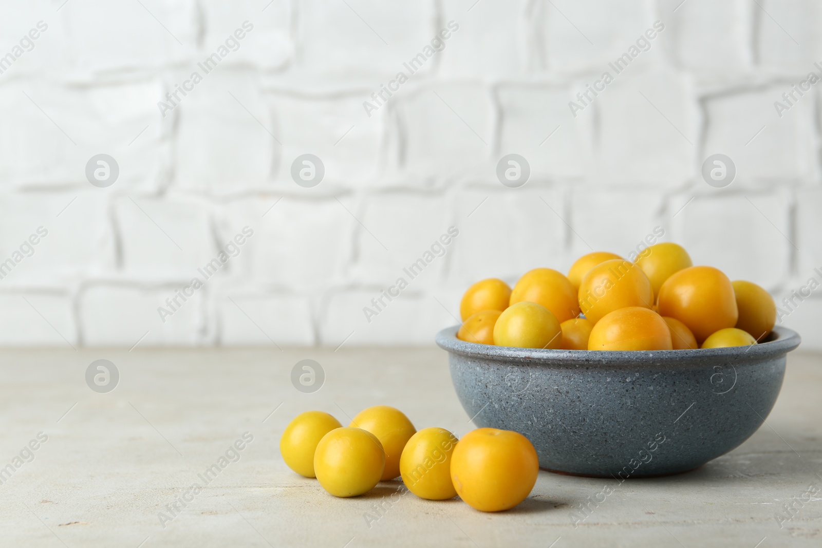 Photo of Ripe plums in bowl on light textured table, space for text