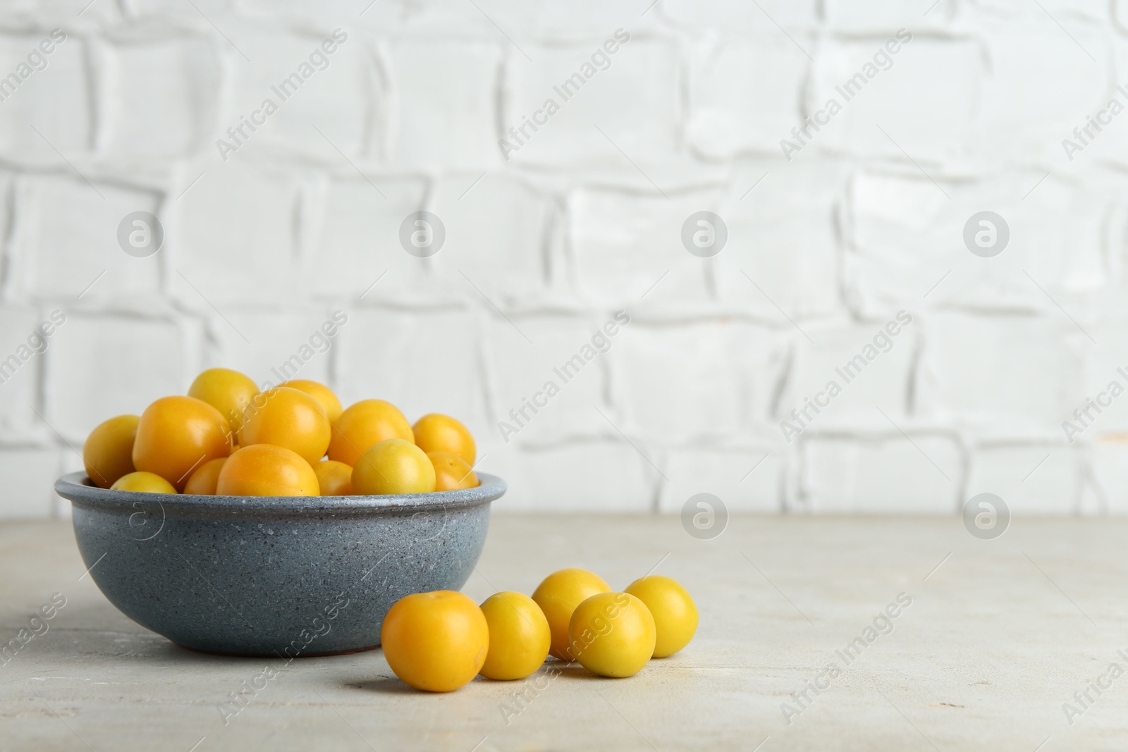 Photo of Ripe plums in bowl on light textured table, space for text