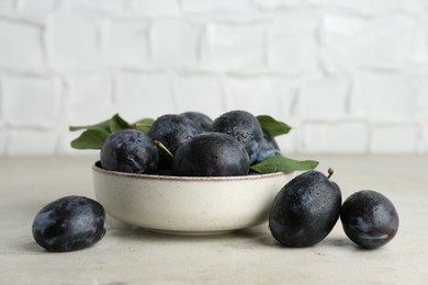 Photo of Ripe plums in bowl on light textured table