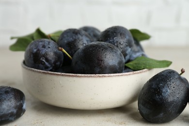 Photo of Ripe plums in bowl on light table, closeup