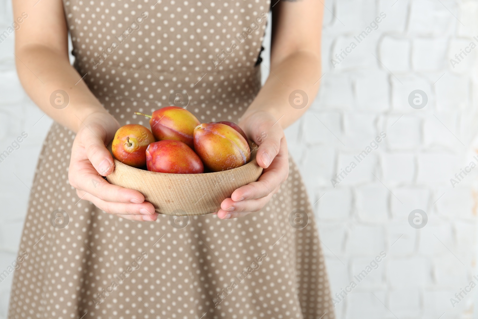 Photo of Woman holding bowl of ripe plums against white background, closeup