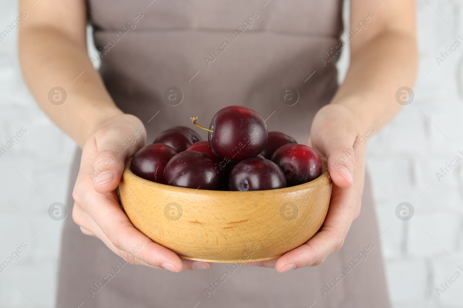 Photo of Woman holding bowl of ripe plums against white background, closeup