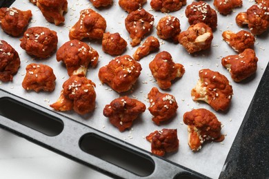 Photo of Tray with tasty cauliflower buffalo wings on white table, closeup