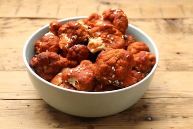 Photo of Tasty cauliflower buffalo wings in bowl on wooden table, closeup