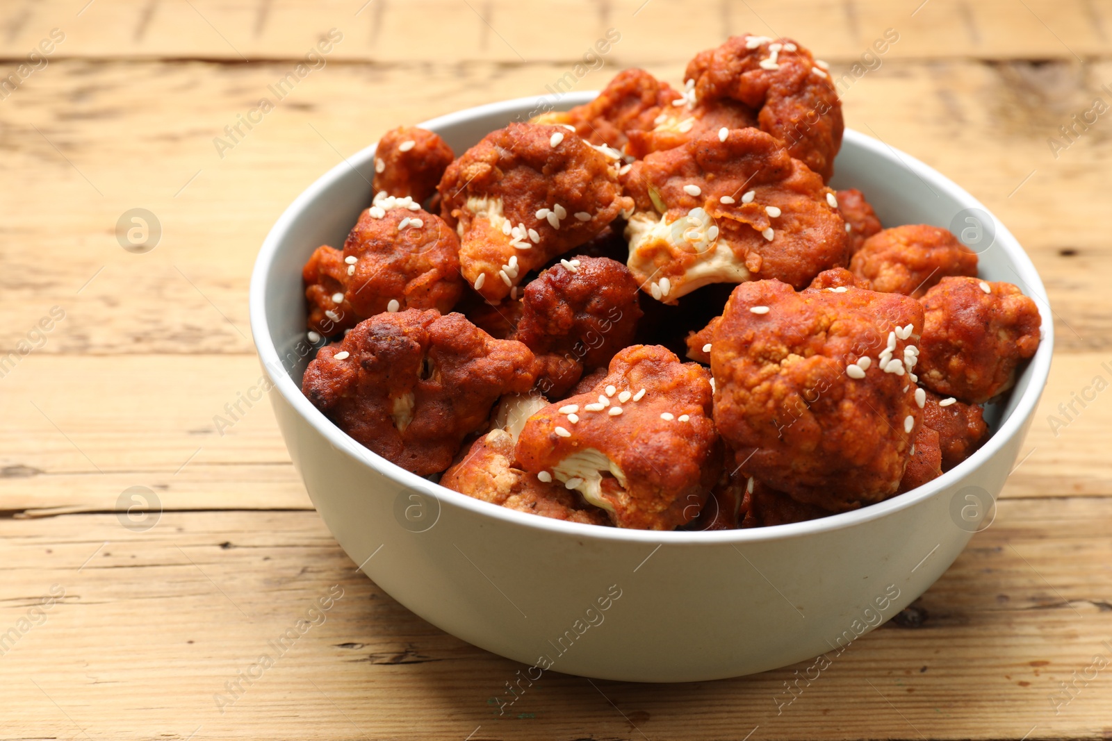 Photo of Tasty cauliflower buffalo wings in bowl on wooden table, closeup