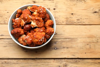 Photo of Tasty cauliflower buffalo wings in bowl on wooden table, top view. Space for text