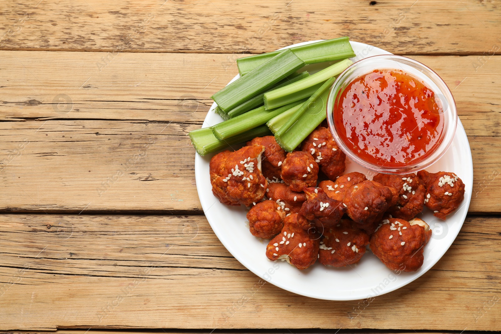 Photo of Tasty cauliflower buffalo wings, sauce and celery on wooden table, top view. Space for text