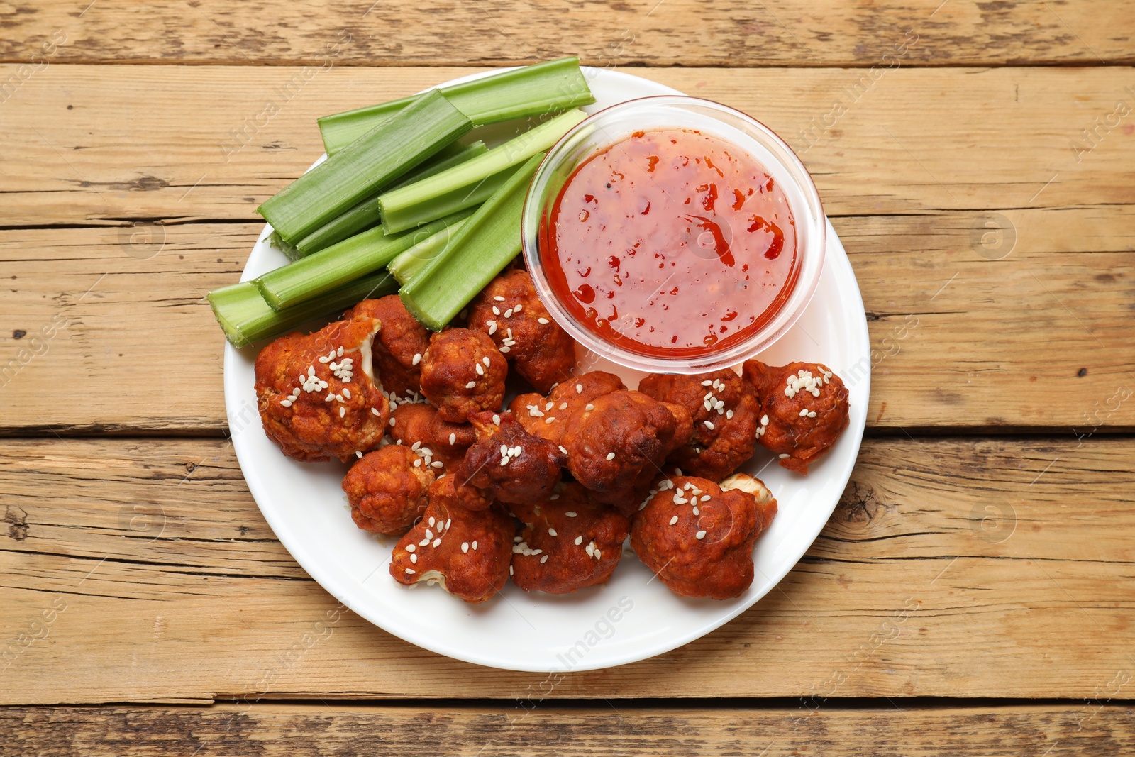 Photo of Tasty cauliflower buffalo wings, sauce and celery on wooden table, top view