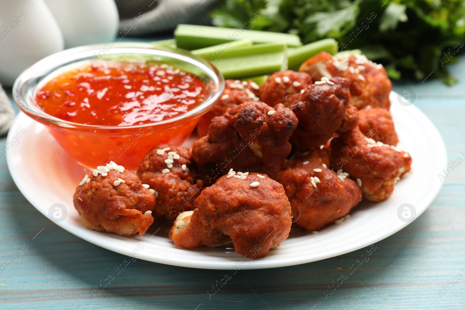 Photo of Tasty cauliflower buffalo wings, sauce and celery on light blue wooden table, closeup