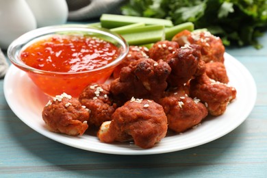 Photo of Tasty cauliflower buffalo wings, sauce and celery on light blue wooden table, closeup