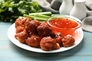 Photo of Tasty cauliflower buffalo wings, sauce and celery on light blue wooden table, closeup