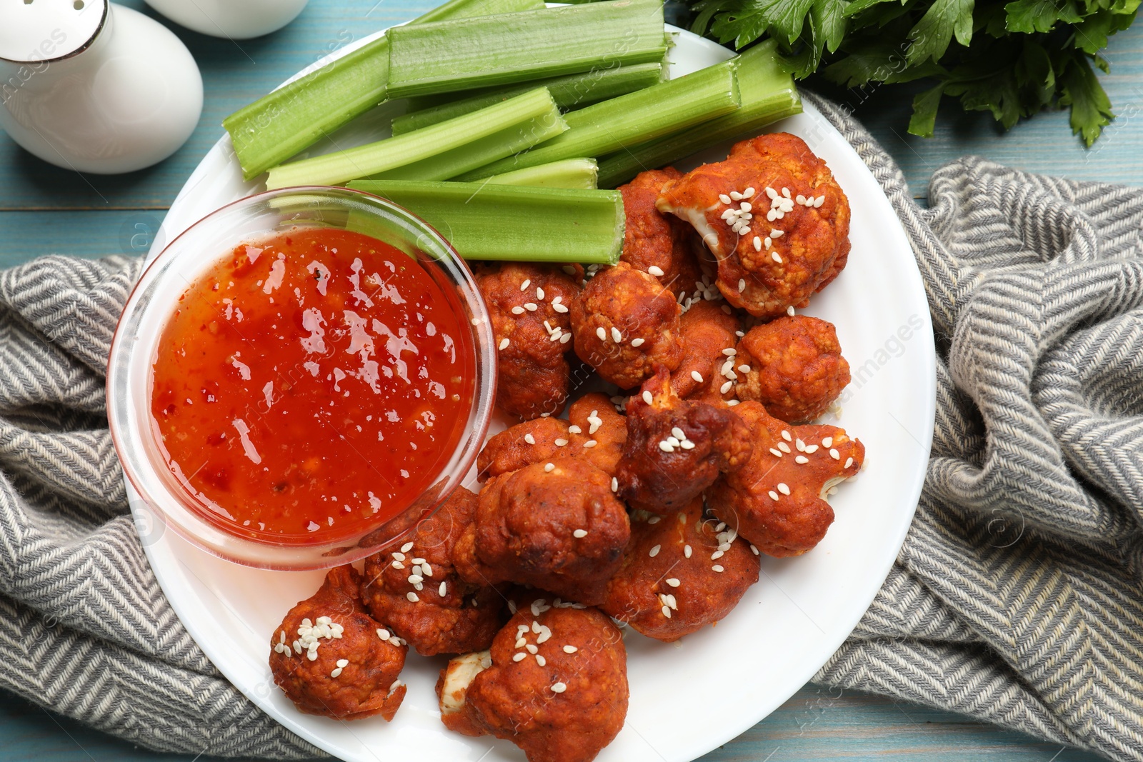 Photo of Tasty cauliflower buffalo wings, sauce and celery on light blue wooden table, flat lay