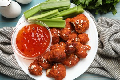 Photo of Tasty cauliflower buffalo wings, sauce and celery on light blue wooden table, flat lay