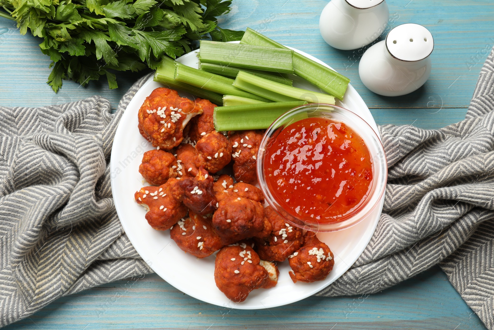 Photo of Tasty cauliflower buffalo wings, sauce and celery on light blue wooden table, flat lay