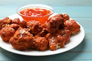 Photo of Tasty cauliflower buffalo wings and sauce on light blue wooden table, closeup