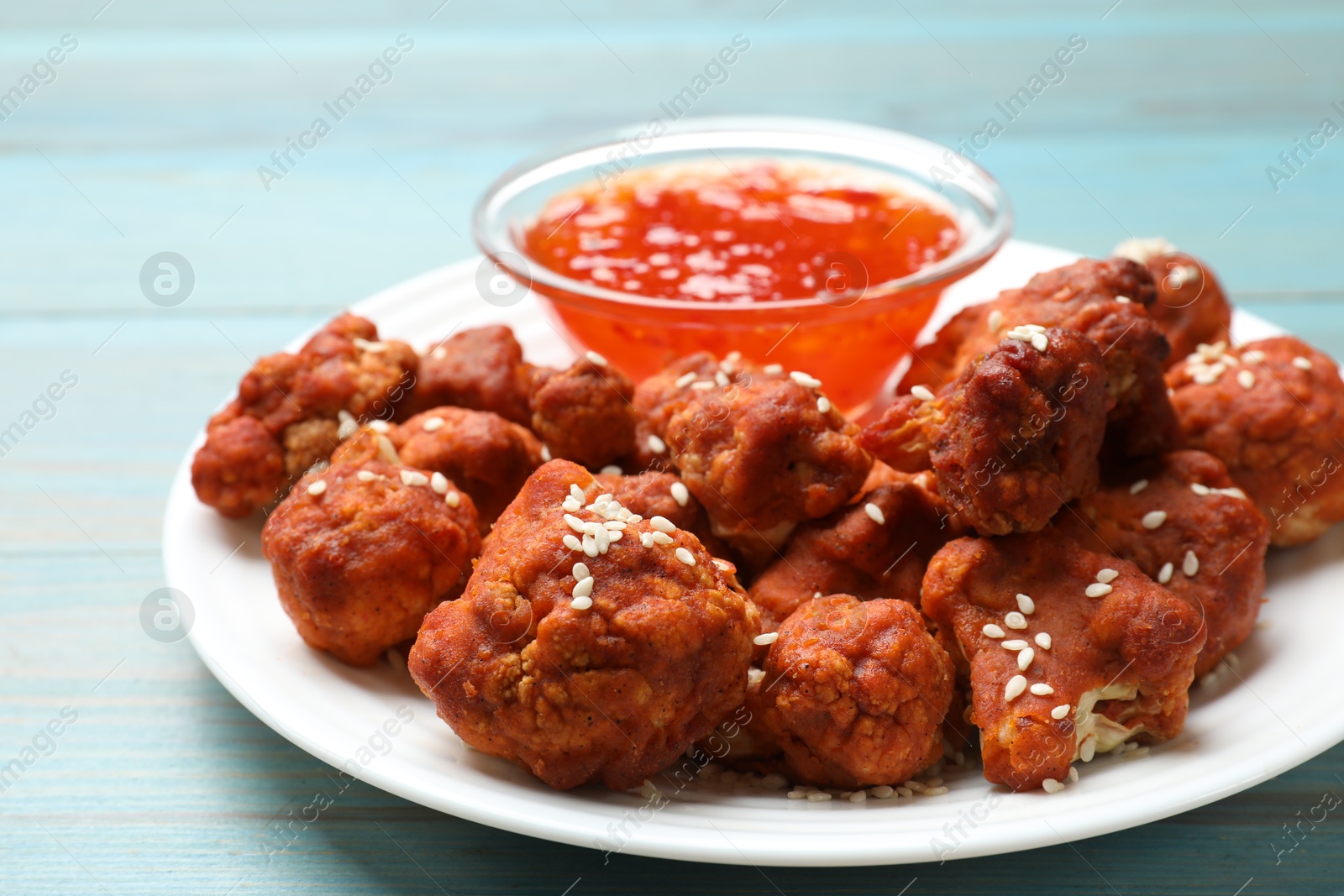 Photo of Tasty cauliflower buffalo wings and sauce on light blue wooden table, closeup