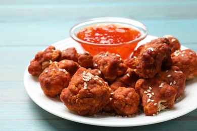 Photo of Tasty cauliflower buffalo wings and sauce on light blue wooden table, closeup