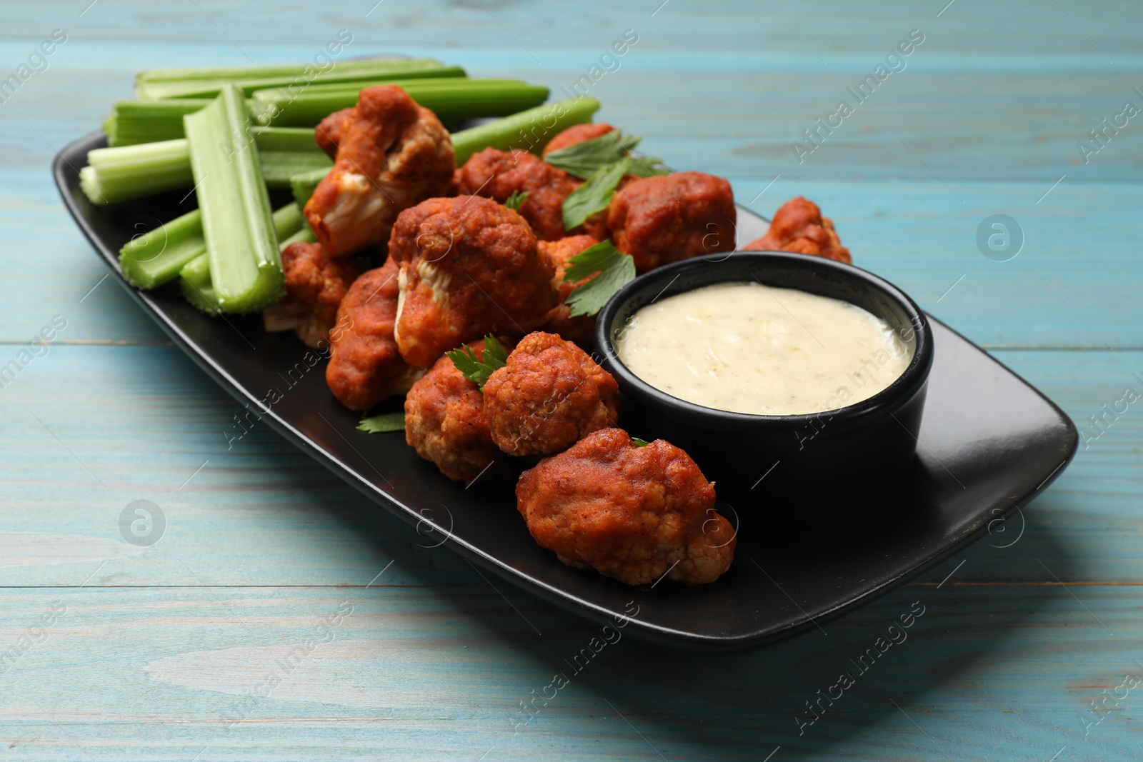 Photo of Tasty cauliflower buffalo wings, sauce and celery on light blue wooden table, closeup