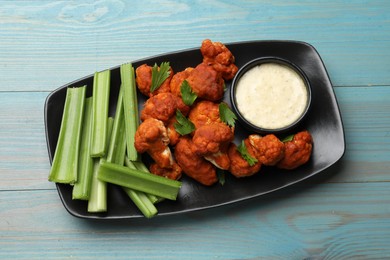 Photo of Tasty cauliflower buffalo wings, sauce and celery on light blue wooden table, top view