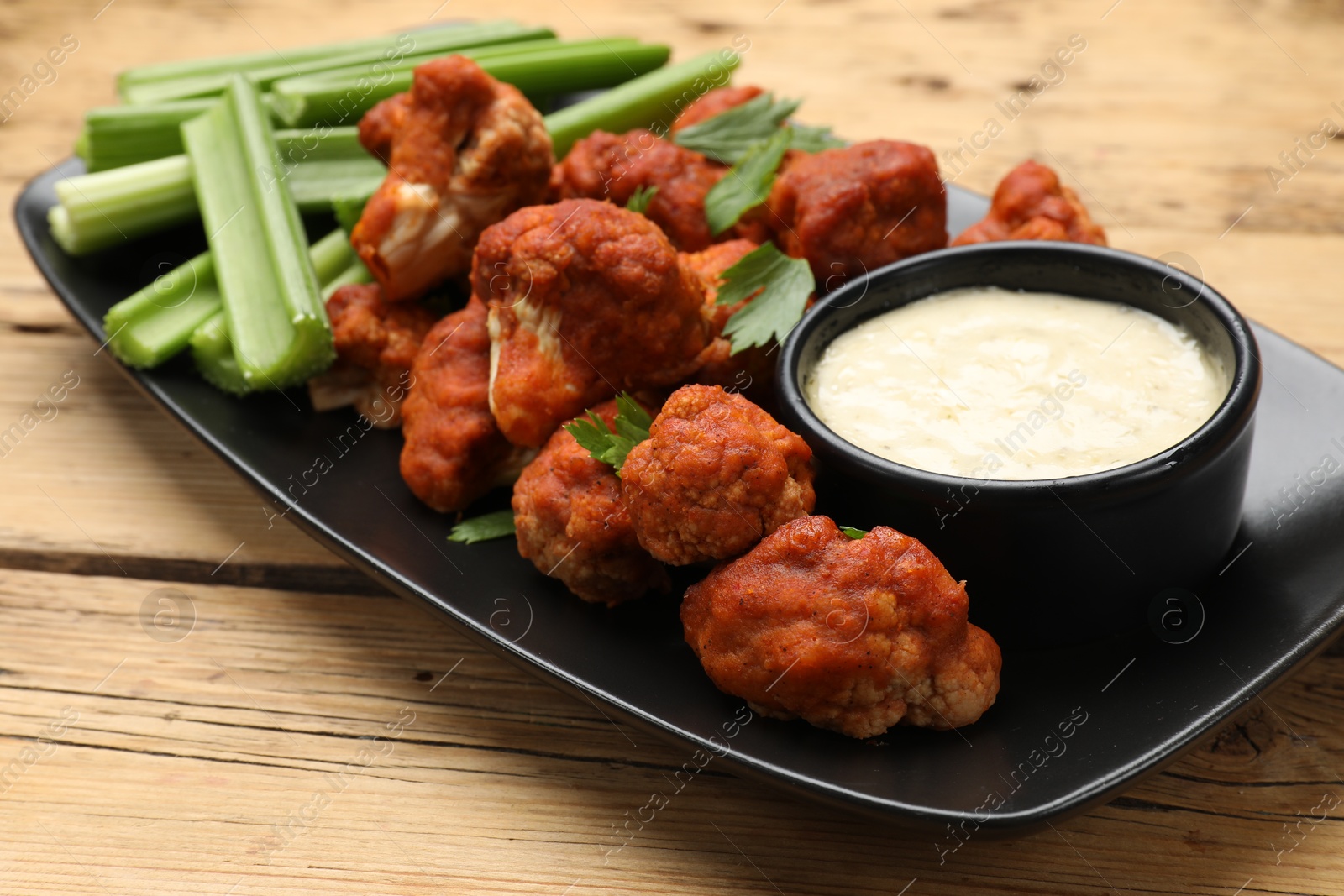 Photo of Tasty cauliflower buffalo wings, sauce and celery on wooden table, closeup