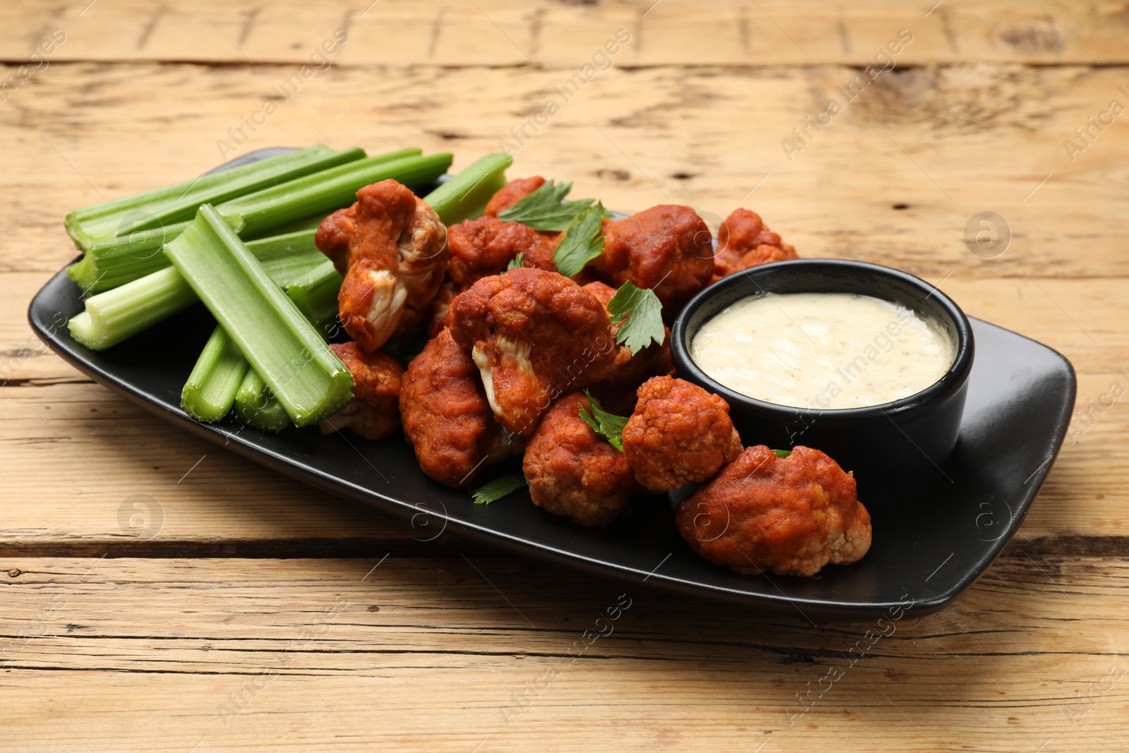 Photo of Tasty cauliflower buffalo wings, sauce and celery on wooden table