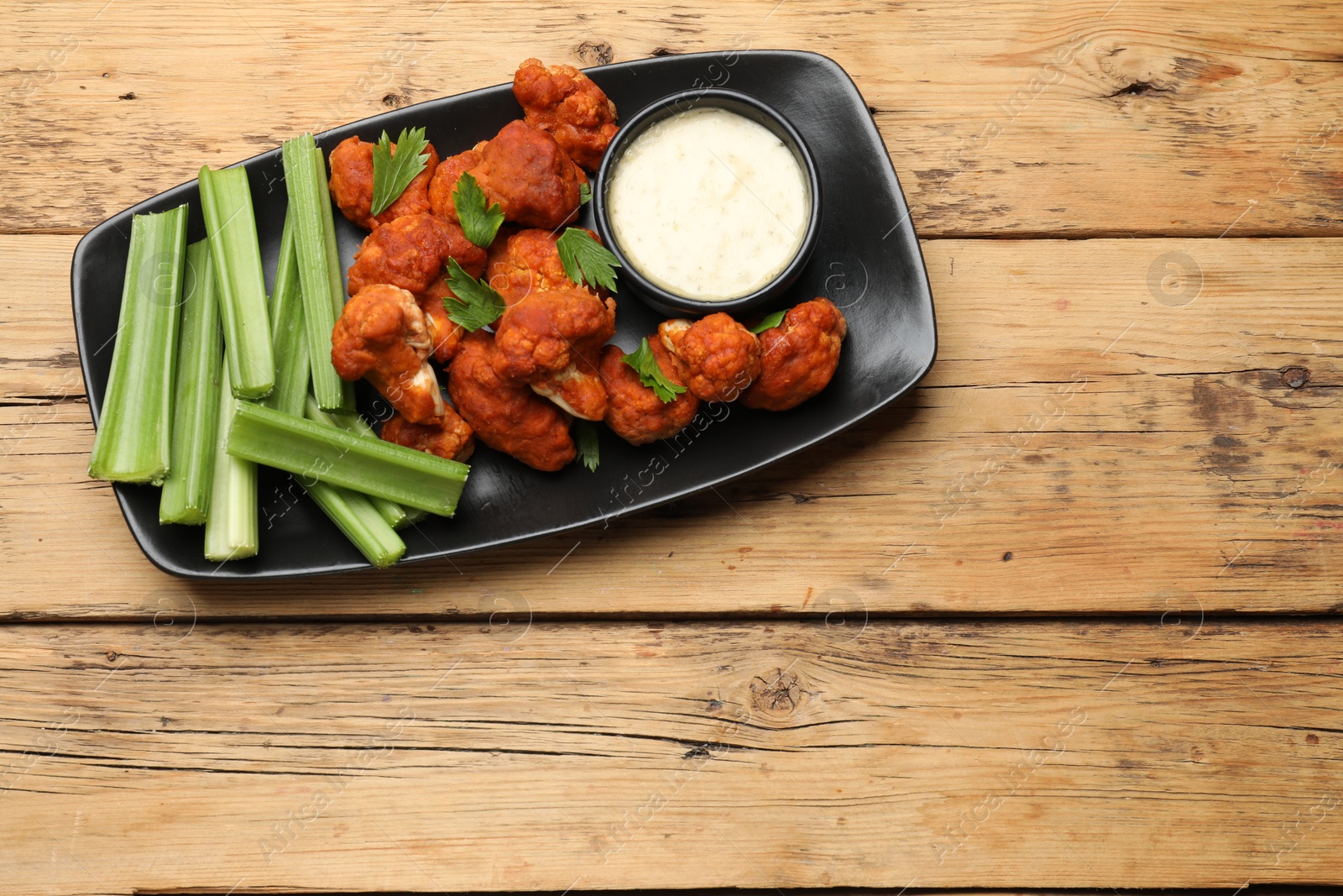 Photo of Tasty cauliflower buffalo wings, sauce and celery on wooden table, top view. Space for text