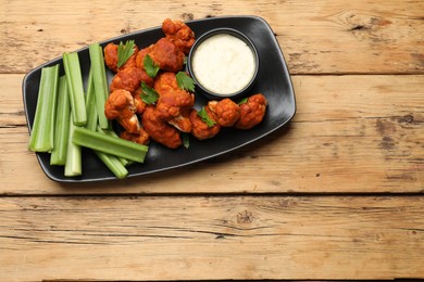 Photo of Tasty cauliflower buffalo wings, sauce and celery on wooden table, top view. Space for text