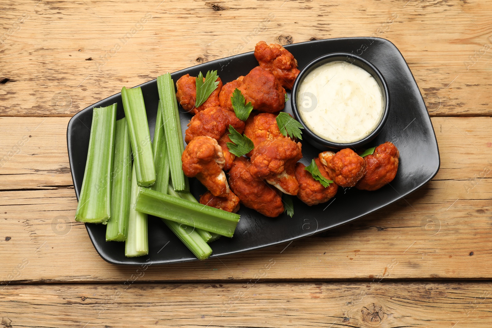 Photo of Tasty cauliflower buffalo wings, sauce and celery on wooden table, top view