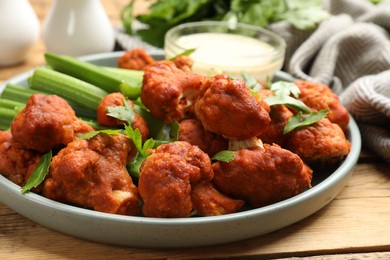 Photo of Tasty cauliflower buffalo wings, sauce and celery on wooden table, closeup