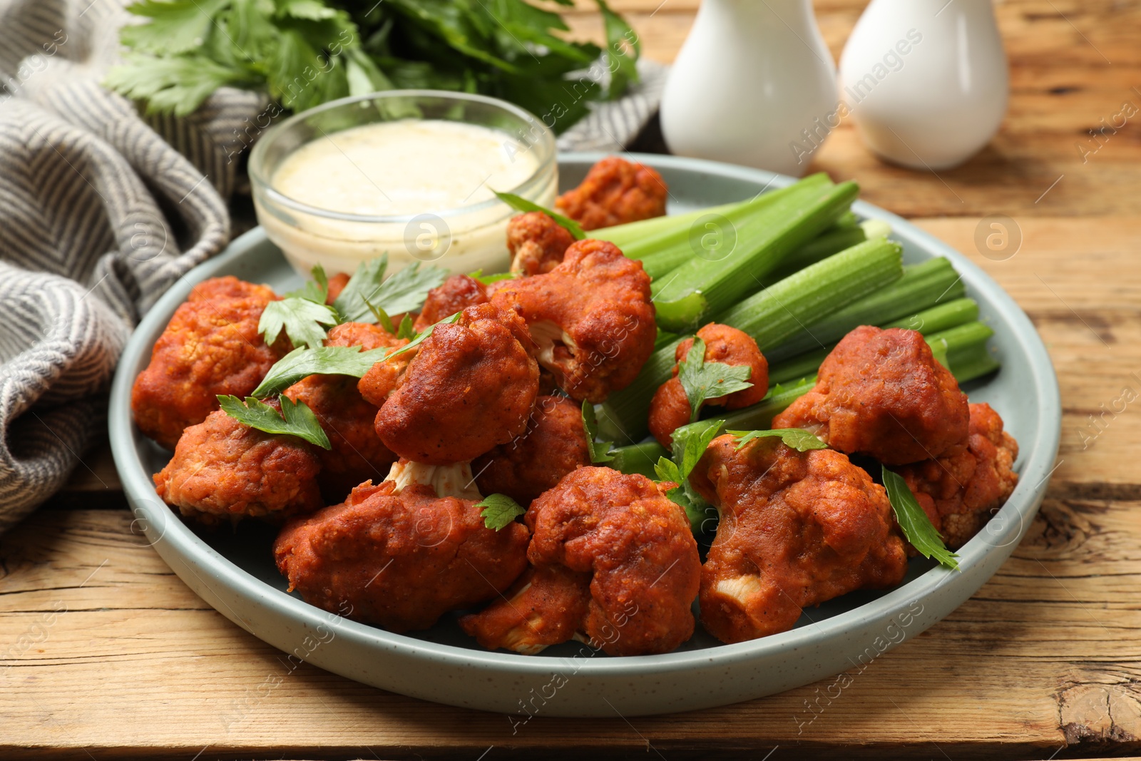 Photo of Tasty cauliflower buffalo wings, sauce and celery on wooden table, closeup