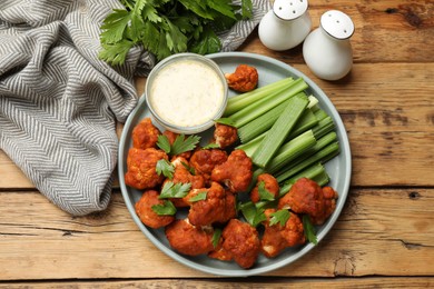 Photo of Tasty cauliflower buffalo wings, sauce and celery on wooden table, flat lay