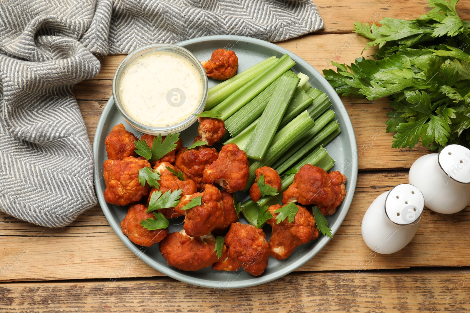 Photo of Tasty cauliflower buffalo wings, sauce and celery on wooden table, top view