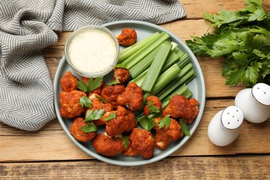 Photo of Tasty cauliflower buffalo wings, sauce and celery on wooden table, top view