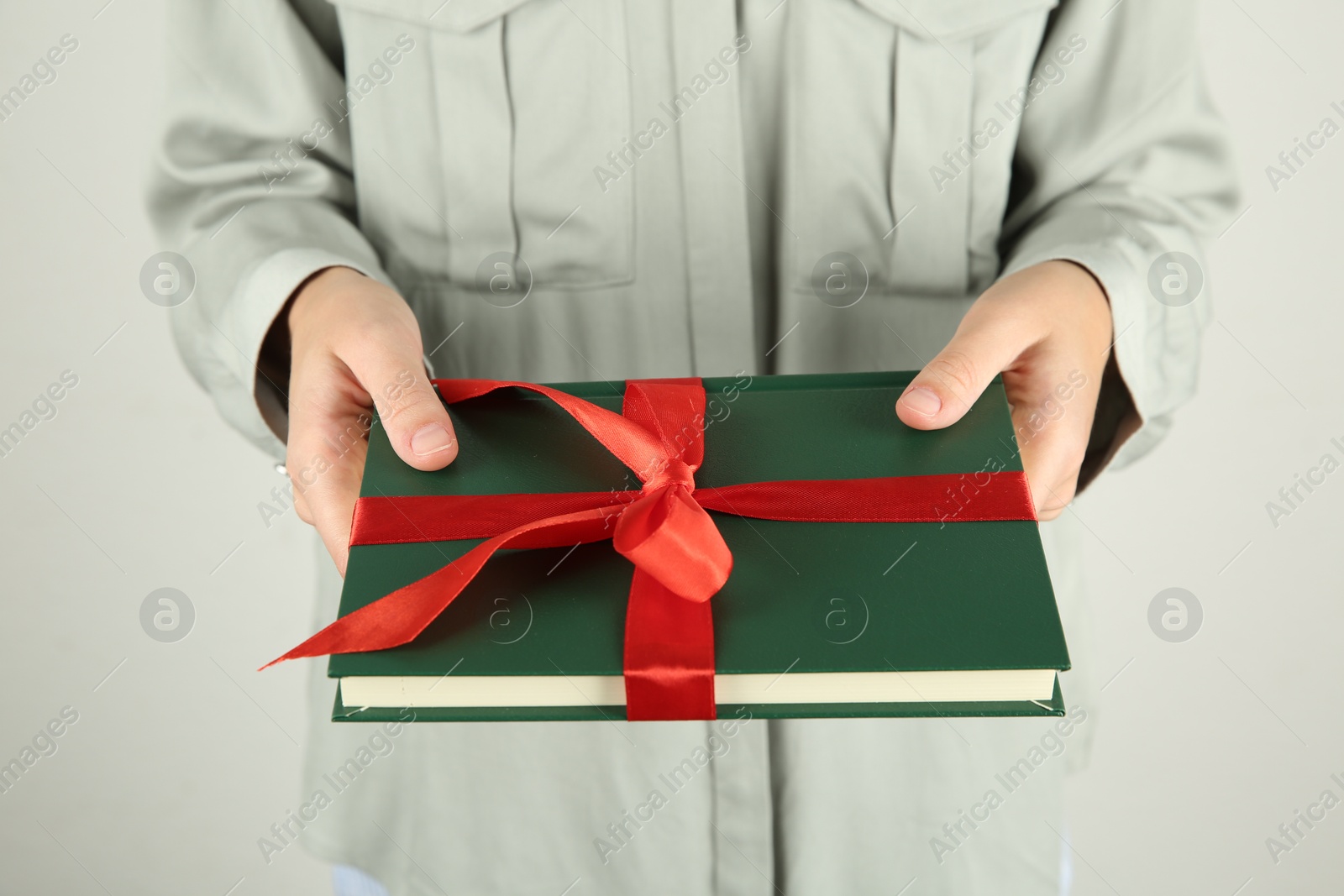 Photo of Woman holding book with ribbon as gift on light grey background, closeup