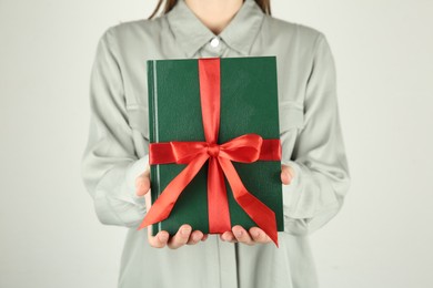 Photo of Woman holding book with ribbon as gift on light grey background, closeup