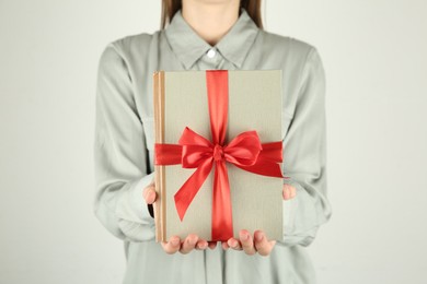 Photo of Woman holding book with ribbon as gift on light grey background, closeup