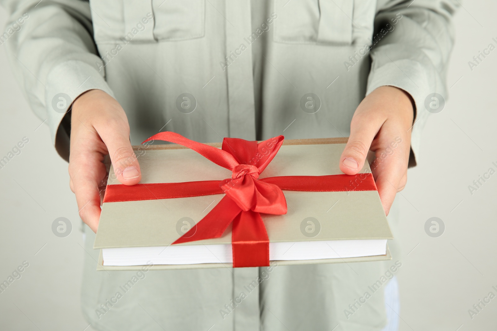 Photo of Woman holding book with ribbon as gift on light grey background, closeup