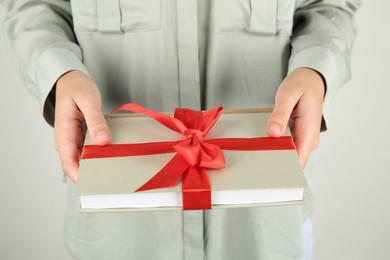 Photo of Woman holding book with ribbon as gift on light grey background, closeup