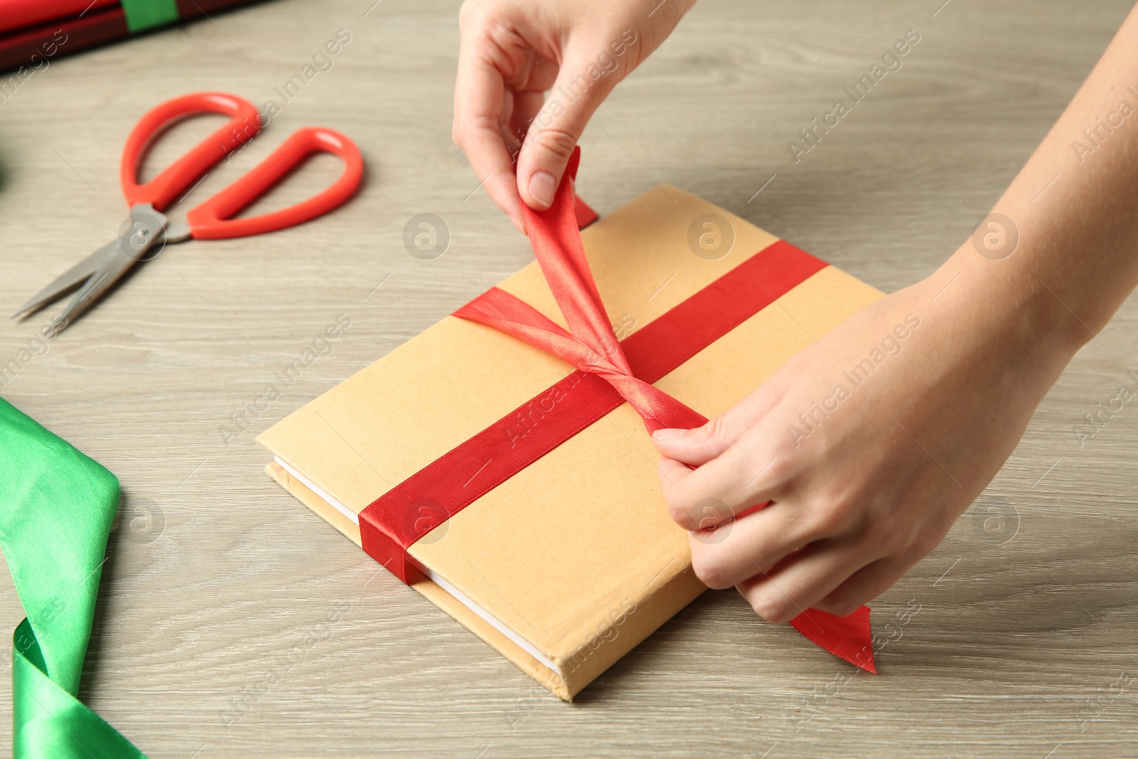 Photo of Woman tying ribbon on book at wooden table, closeup