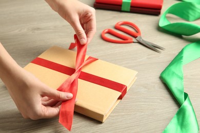 Photo of Woman tying ribbon on book at wooden table, closeup