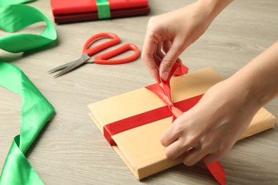 Photo of Woman tying ribbon on book at wooden table, closeup