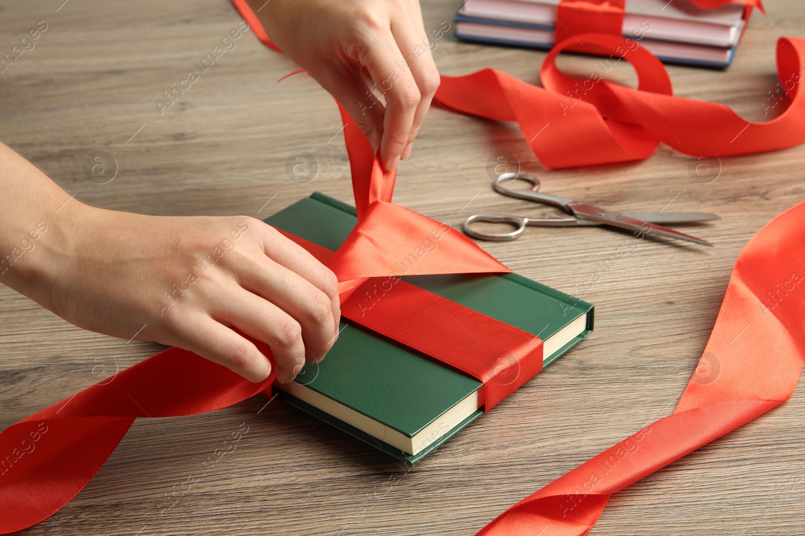 Photo of Woman tying ribbon on book at wooden table, closeup