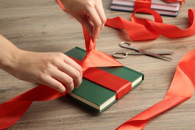 Photo of Woman tying ribbon on book at wooden table, closeup