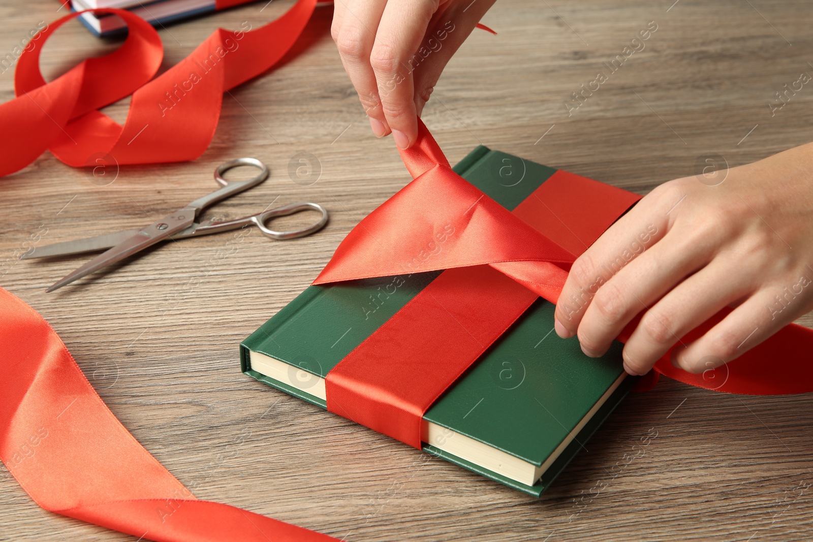 Photo of Woman tying ribbon on book at wooden table, closeup