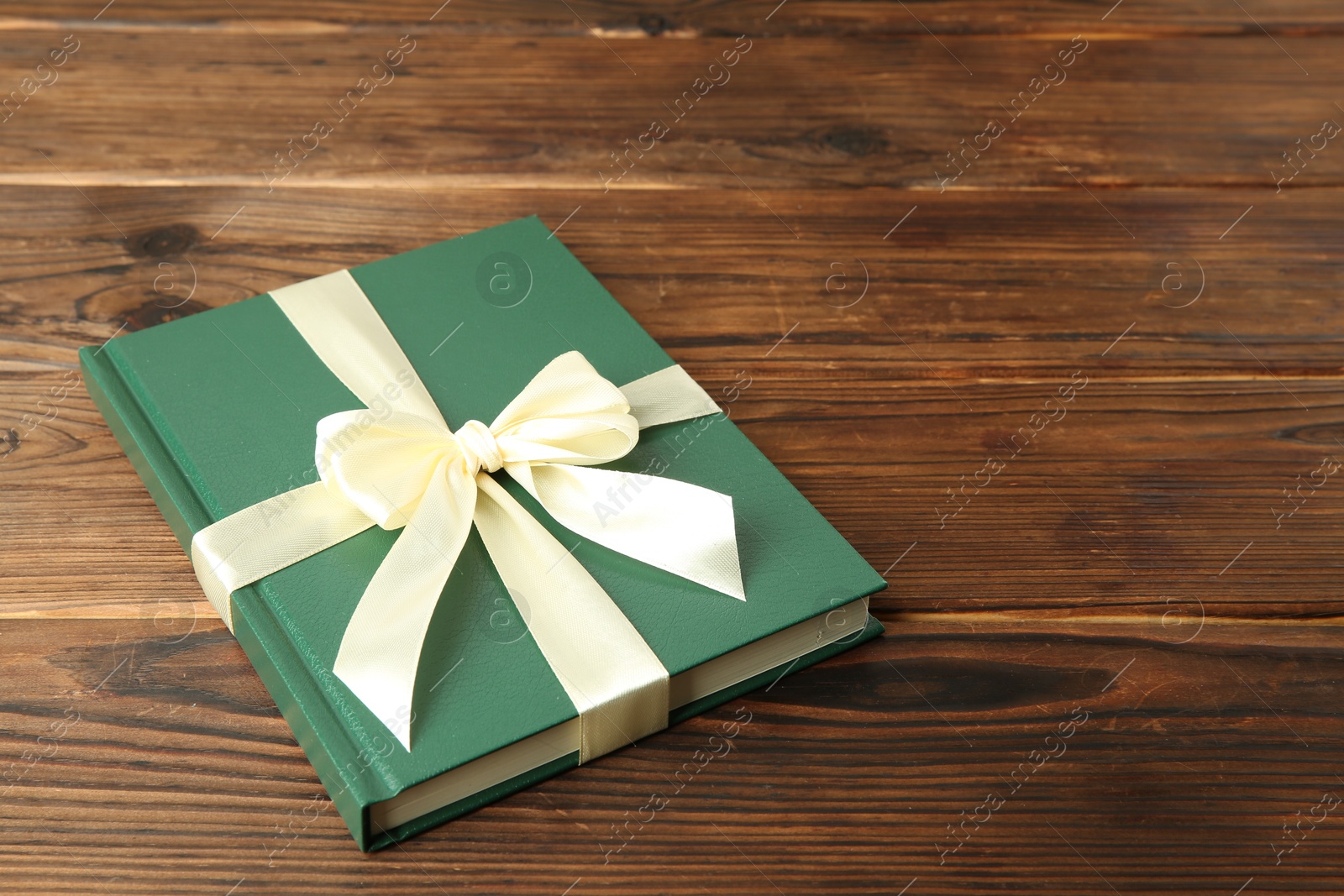 Photo of Book with ribbon as gift on wooden table, space for text