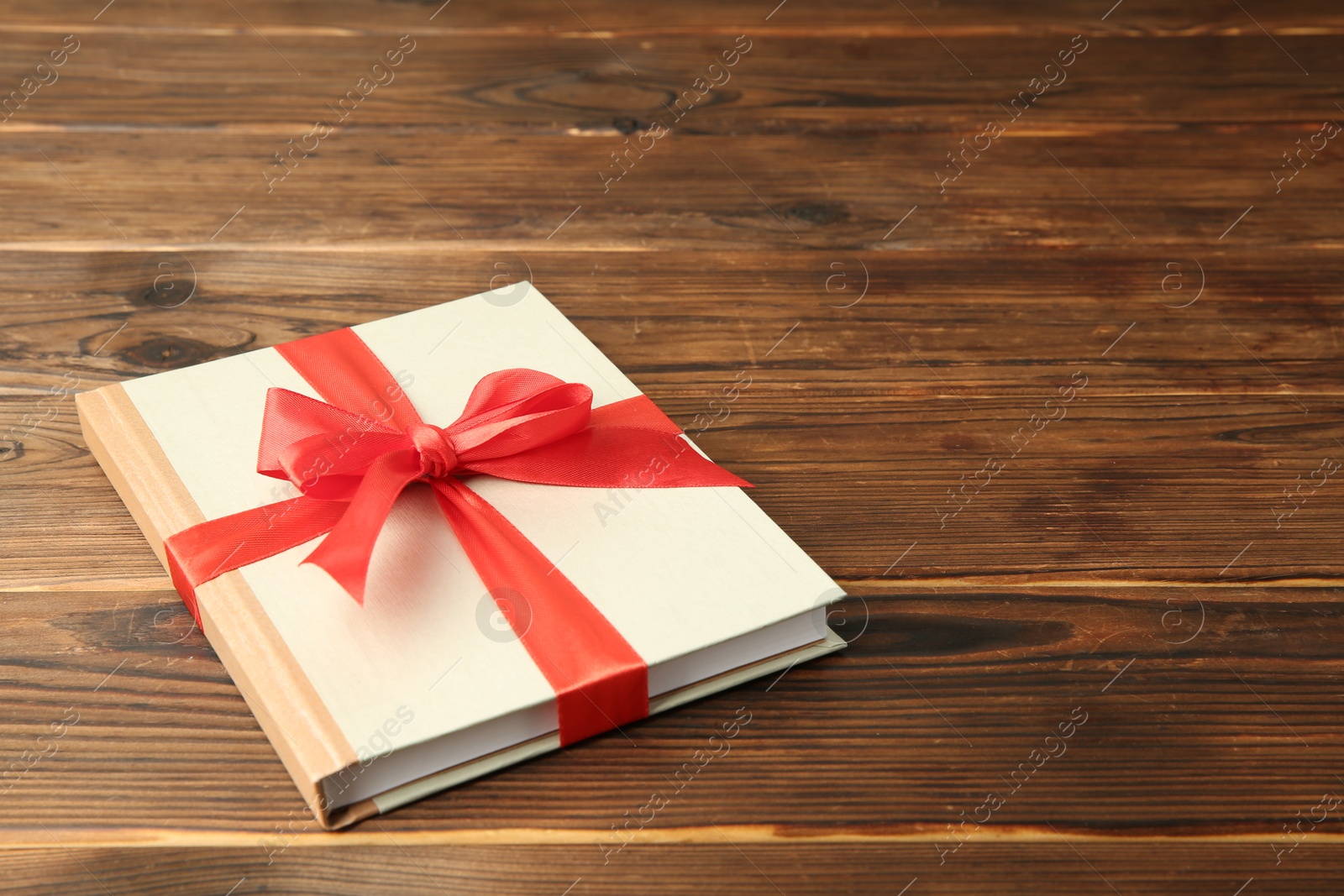 Photo of Book with ribbon as gift on wooden table, space for text